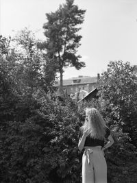 Rear view of woman standing by plants against sky