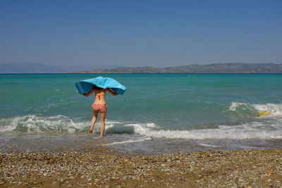 Rear view of woman standing on beach against clear sky