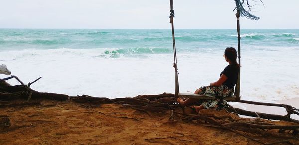 Woman sitting on swing at beach