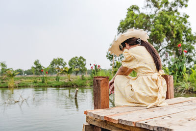 Woman sitting on wood by lake against trees