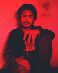 Portrait of young man standing against red background