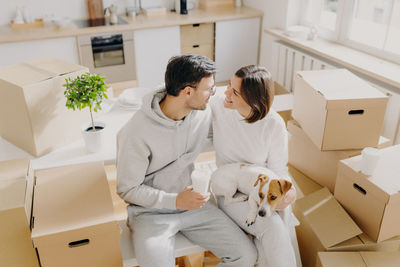 High angle view of romantic couple with dog sitting amidst boxes in new house