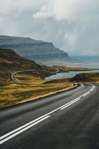 Empty road amidst landscape against cloudy sky