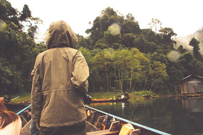Rear view of man wearing jacket traveling in boat on lake