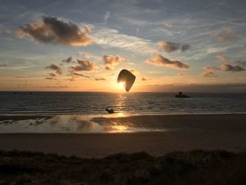 Silhouette person paragliding over beach against sky during sunset