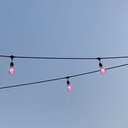 Low angle view of light bulbs hanging against clear sky