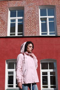 Young woman standing against red building
