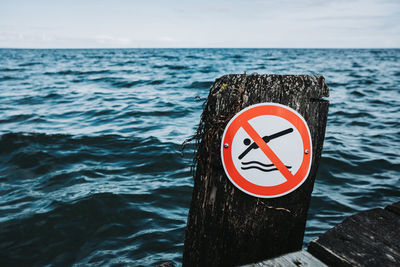 Close-up of sign by wooden post in sea against sky