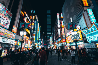 People walking on illuminated street amidst buildings at night