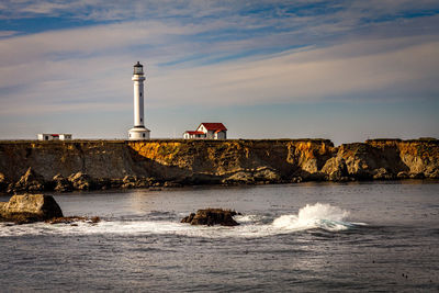 Lighthouse by sea and buildings against sky