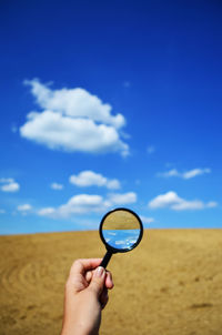 Close-up of hand holding magnifying glass against sky