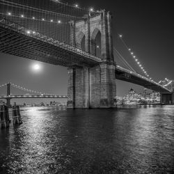 Low angle view of brooklyn bridge over east river in city at night
