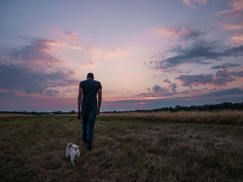 Rear view of man walking with dog on field against sky