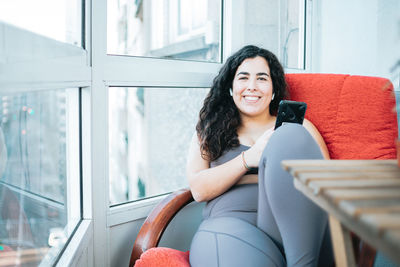 Portrait of young woman using smart phone sitting on sofa at home