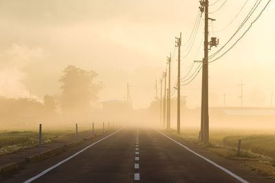 Road by electricity pylon against sky