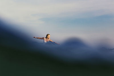 Distant view of woman surfboarding in sea against sky