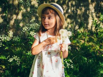 Portrait of girl holding flower standing against plants