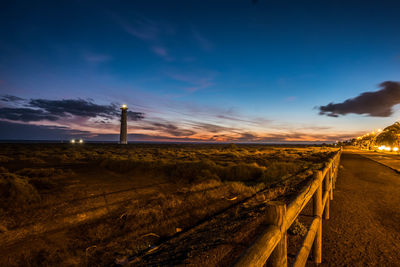 Road by illuminated landscape against sky at night