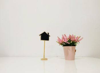 Flowers in pot by blank sign on table against white wall