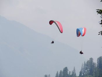 Low angle view of people paragliding against sky