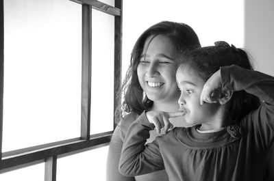 Smiling mother with daughter by window at home