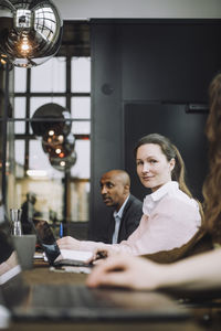 Portrait of mid adult businesswoman sitting with laptop by colleagues in meeting room
