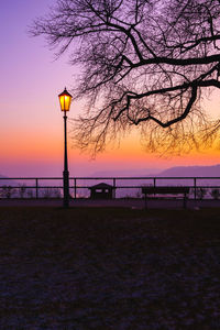 Silhouette street light by sea against sky at sunset