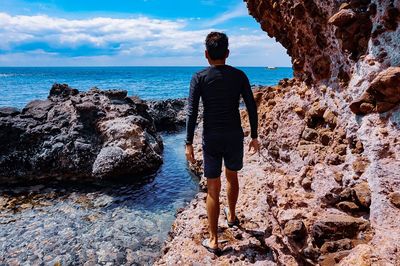 Rear view of man walking on rock at beach