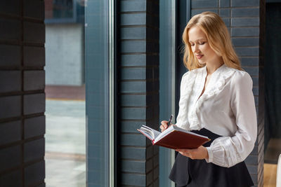 Young woman looking away while standing against window