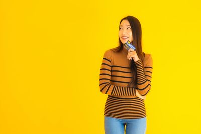 Portrait of young woman standing against yellow background