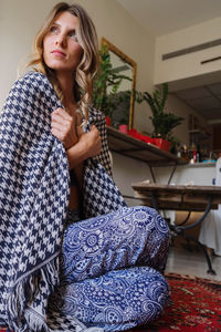 Woman wearing a crystal necklace meditation at home wrapped up in blanket