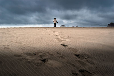 Person alone on top of sand dune at the beach under a dramatic sky.