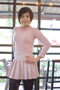 Portrait of a smiling young woman standing against window