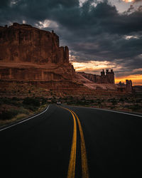 Road leading towards rock formation against sky