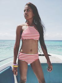 Young woman wearing bikini standing on boat in sea during sunny day