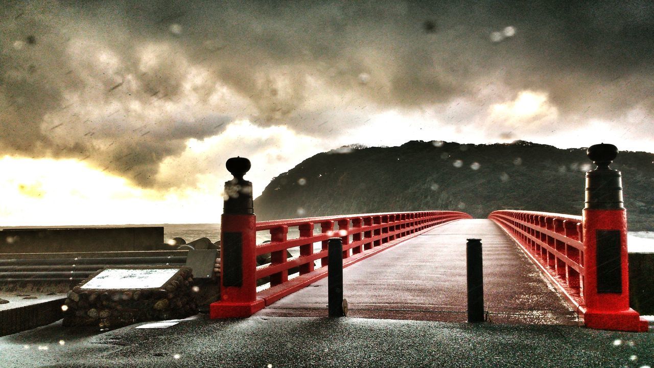 sky, cloud - sky, cloudy, weather, built structure, railing, architecture, overcast, red, water, cloud, bridge - man made structure, transportation, dusk, storm cloud, outdoors, connection, nature, dramatic sky, mountain