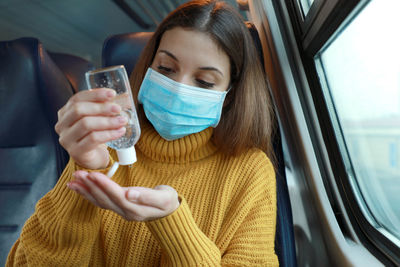 Young woman cleaning hand while using hand sanitizer sitting at bus