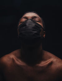 Close-up of shirtless man wearing mask against black background