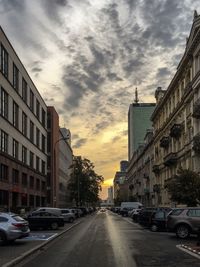 Cars on city street against cloudy sky