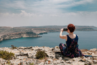 Rear view of woman photographing on cliff against sea