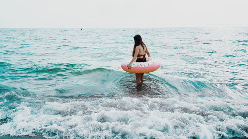 Woman with inflatable ring wading in sea against clear sky