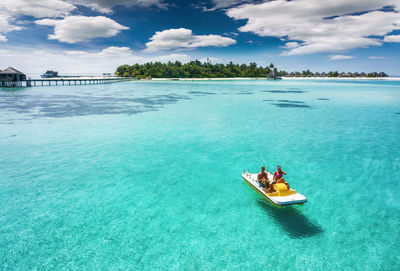 Couple pedaling boat on sea against sky