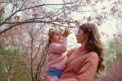 Mother and little daughter, standing in the park under a blossom tree