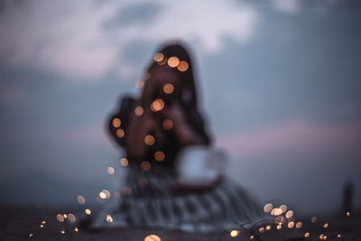 Defocused image of illuminated christmas lights against sky at dusk