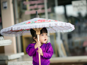 Close-up of cute girl holding umbrella while standing outdoors