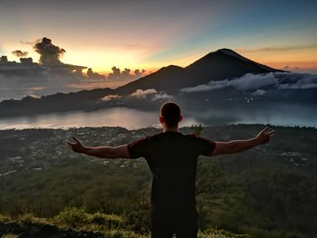 Rear view of man standing on mountain against sky