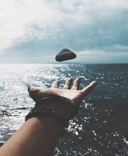 Cropped hand reaching rock over sea against sky