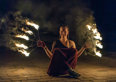 Portrait of fire dancer holding burning equipment at night