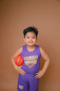 Portrait of boy playing basketball while standing against wall
