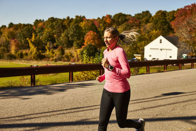 A close up of a woman running down a country road on a fall day.